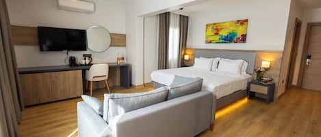 A modern hotel room with a bed, a sofa, a desk, a television, and a painting on the wall.