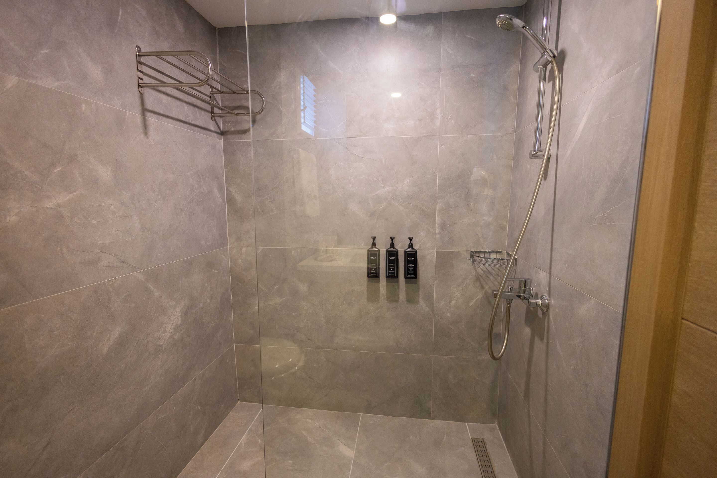 A walk-in shower with a glass door, a metal towel rack, and two bottles of shampoo and conditioner on the wall.