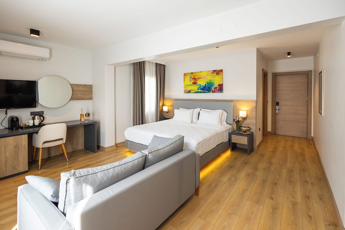 A modern hotel room with a bed, a sofa, a desk, a TV, and a painting on the wall.