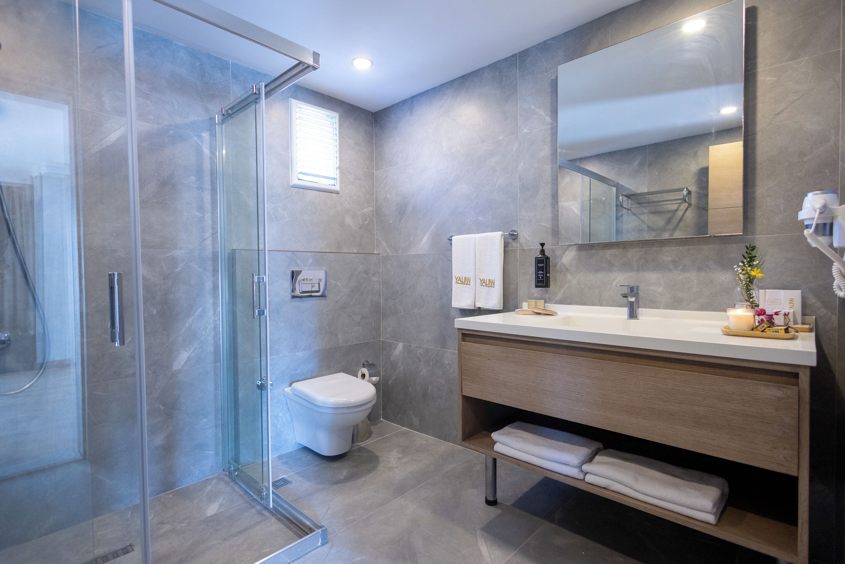 A modern bathroom with a glass shower enclosure, a toilet, a sink with a mirror, and a vanity with towels.