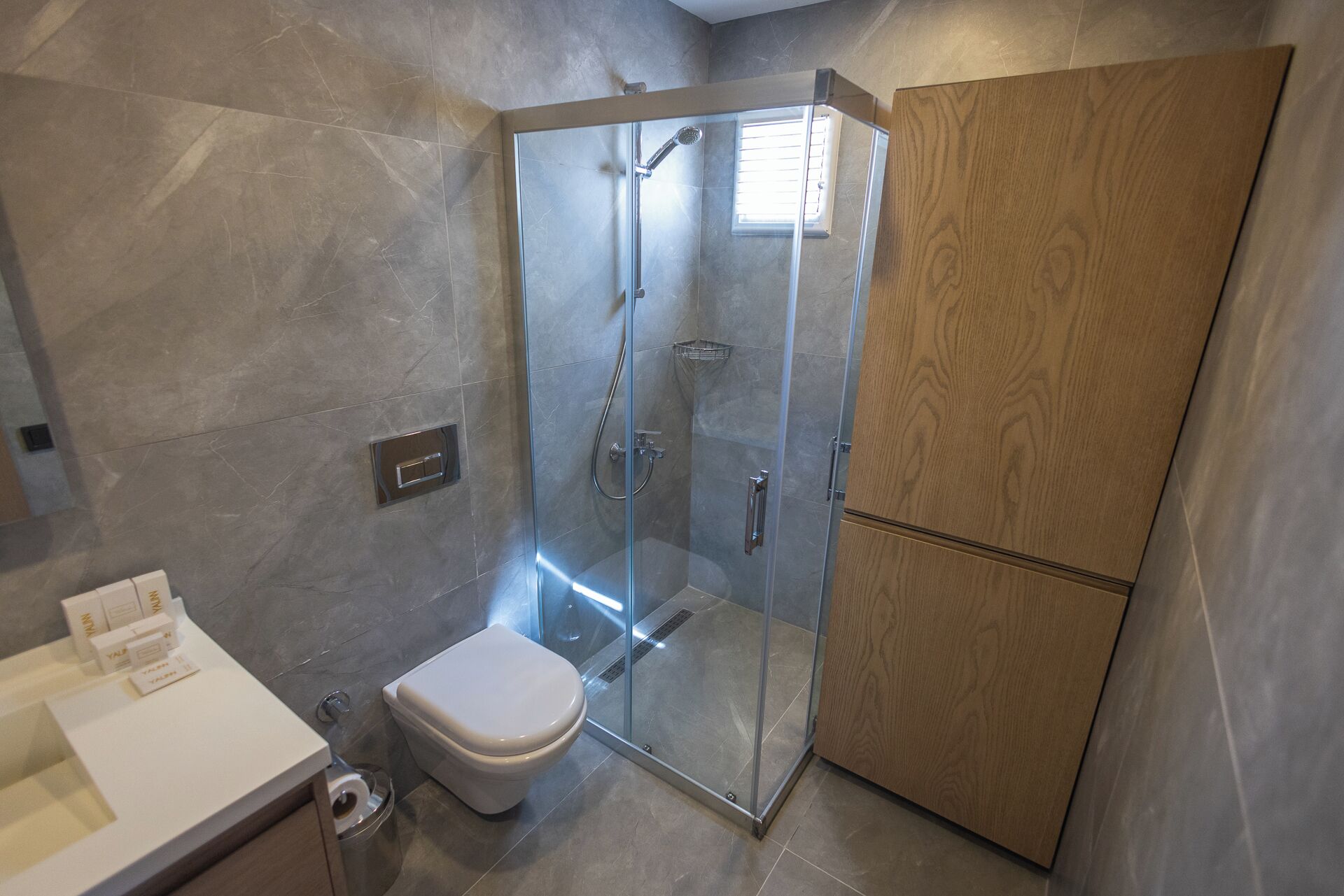 Une salle de bain moderne avec une douche à parois de verre, des toilettes blanches et un meuble en bois.