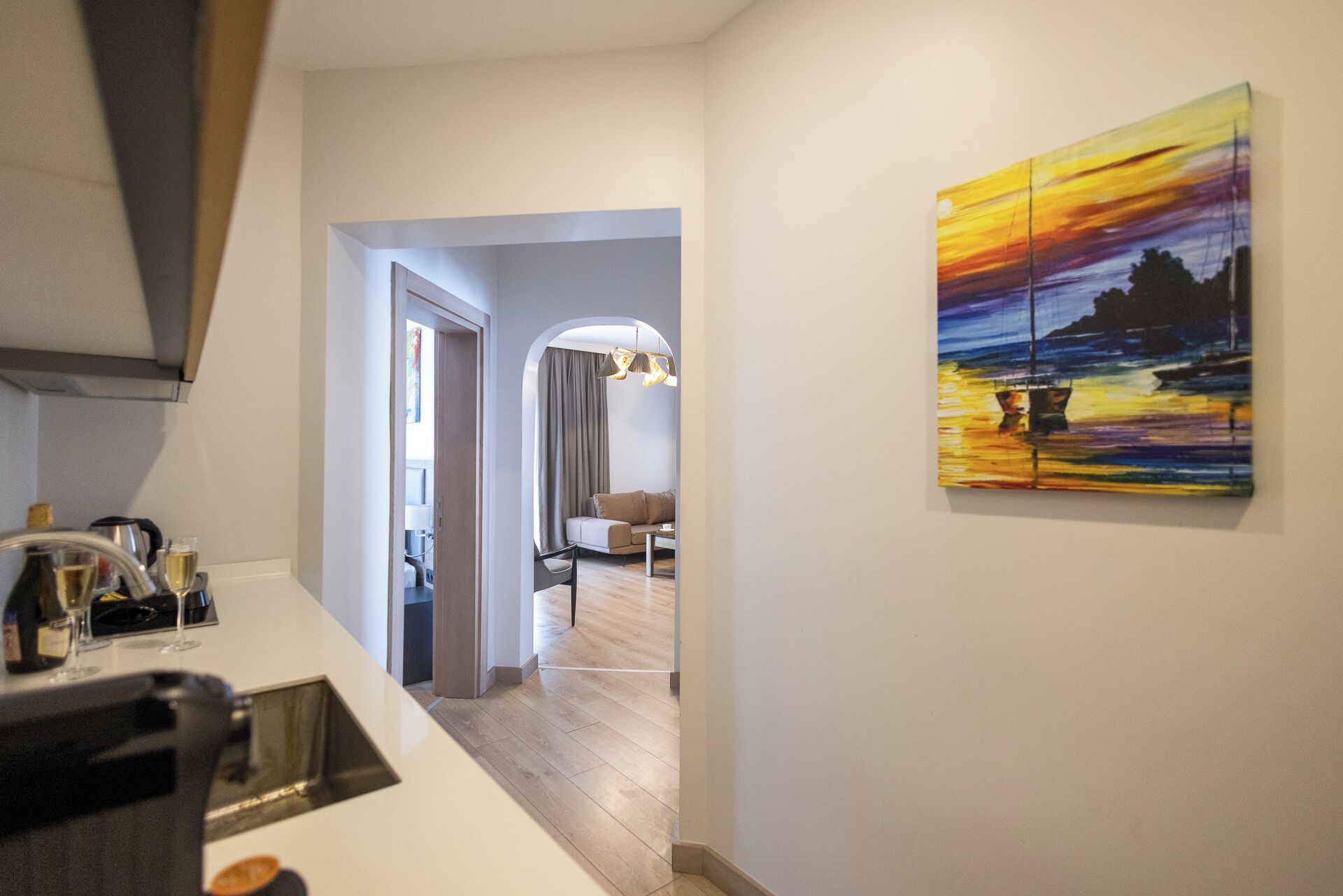 A modern kitchen with a dining area, a hallway leading to a living room, and a painting on the wall.