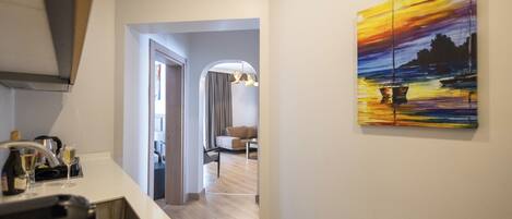 A modern kitchen with a dining area, a hallway leading to a living room, and a painting on the wall.