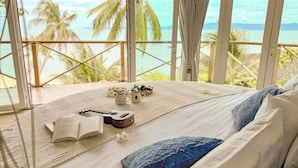 Ein Bett mit Blick auf den Ozean, ein Buch, eine Ukulele und eine Tasse mit Katzenmotiv.
