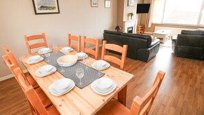 Un comedor con una mesa de madera dispuesta para seis personas, rodeada de sillas a juego. En el fondo, un sofá negro y un sofá de cuero negro.