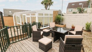 Un patio exterior con mobiliario de mimbre, cerramiento de cristal y terraza de madera.