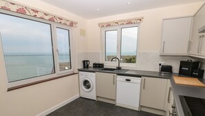 Una cocina moderna con lavadora, lavavajillas y vistas al mar a través de amplios ventanales.