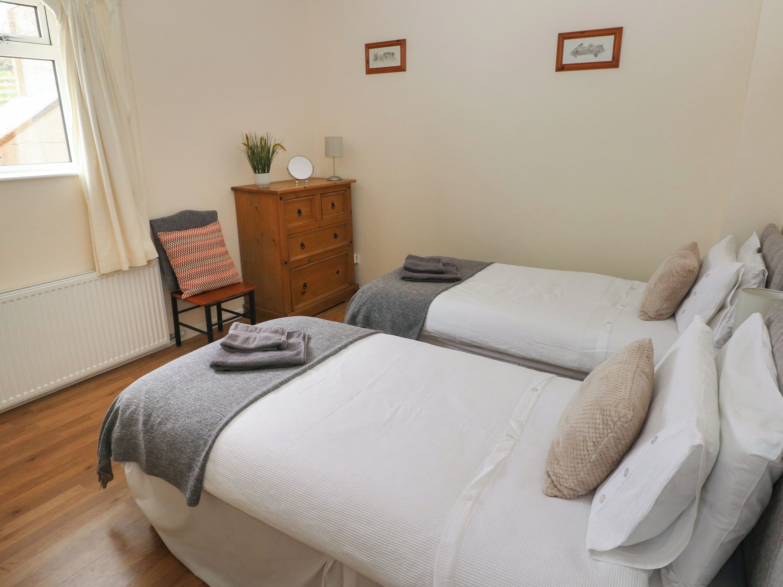 Un dormitorio con dos camas, un aparador de madera, una silla y una ventana con cortinas.