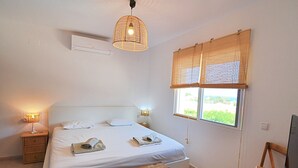 Un dormitorio con cama, lámparas de noche, un banco de madera, un televisor y una ventana con vistas.