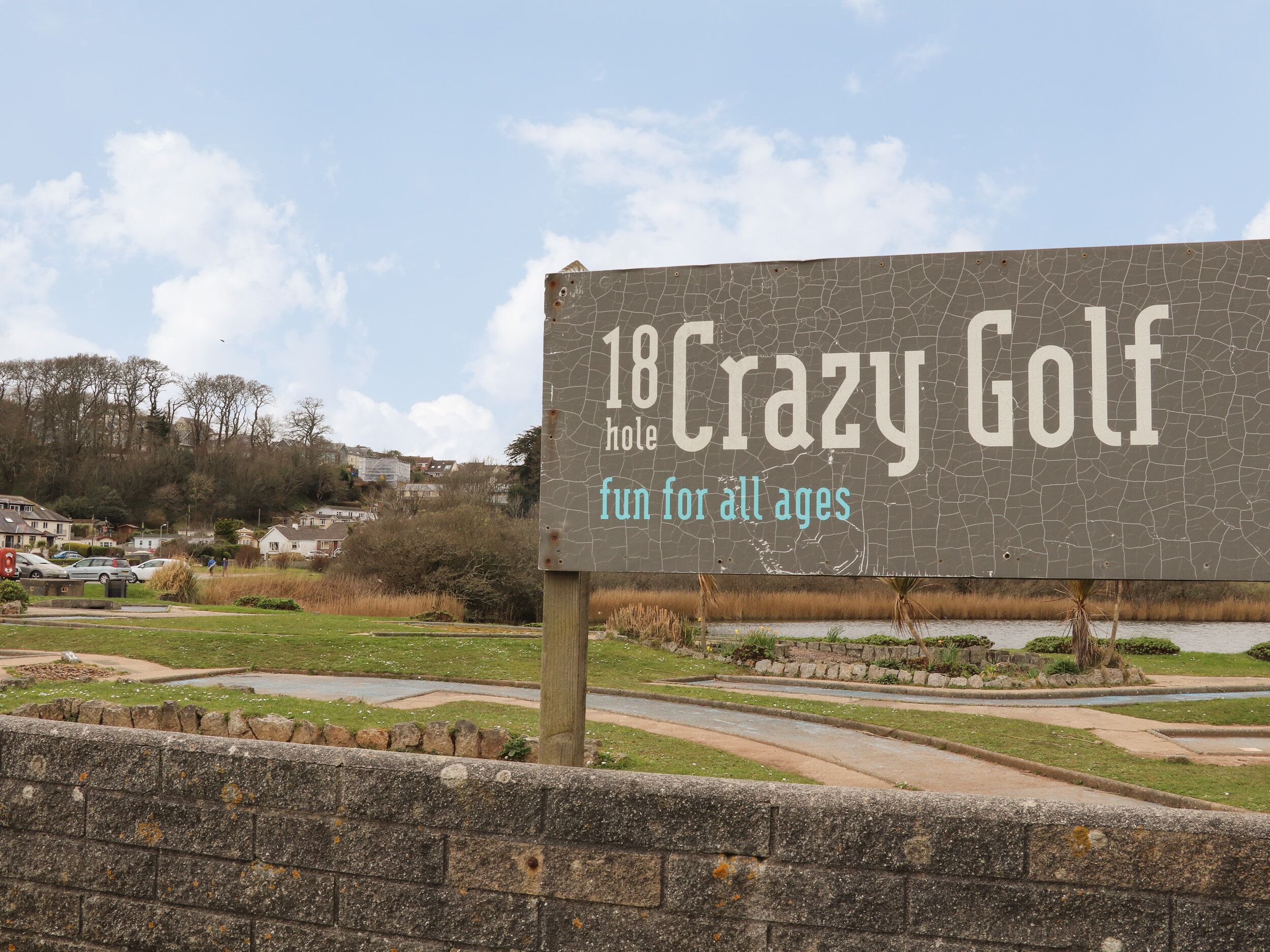 A sign for '18 Crazy Golf' with a cracked surface, indicating a hole golf course.