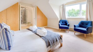 Quarto com cama grande, poltrona azul, guarda-roupa de madeira e área de chuveiro.