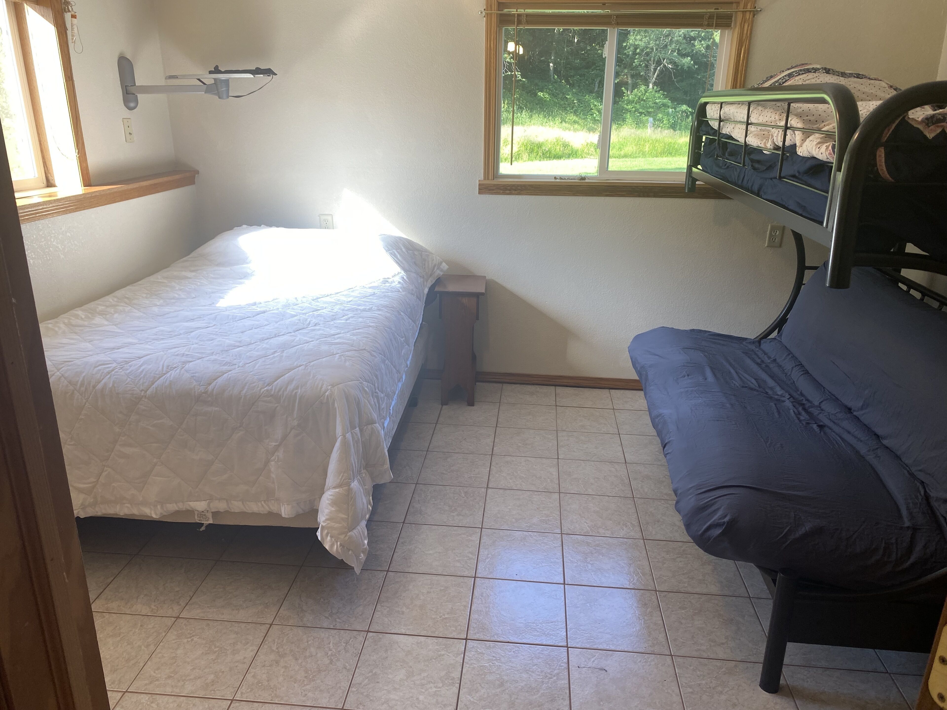 Une chambre avec un lit, une petite table, une fenêtre donnant sur un paysage verdoyant et un banc.