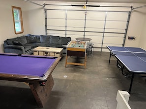 Une pièce équipée d’une table de billard, d’un baby-foot, d’une table de ping-pong, d’un canapé et d’une table de tennis de table.
