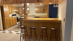 A kitchen with wooden cabinets, a central island with stools, a stove, and a sink. - Private vacation house for larger groups near the Dells with heated game room. (Reedsburg)