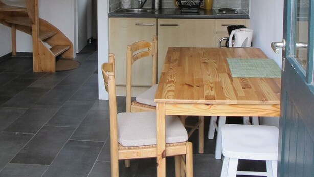 Een keuken met houten kastjes, een eettafel en een trap.