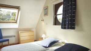 Een slaapkamer met een bed, een stoel, een dressoir, een raam en een lamp.