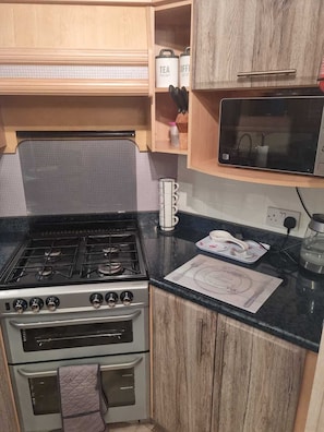 A kitchen with a gas stove, oven, microwave, and wooden cabinets. - Discover Comfort Home From Home 8-birth Caravan (Skegness)