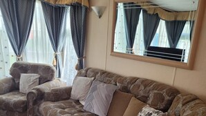 A living room with a sofa set, a mirror, and a hand sanitizer bottle. - Discover Comfort Home From Home 8-birth Caravan (Skegness)