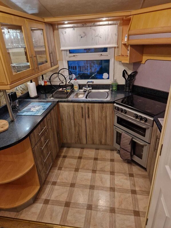 A compact kitchen with wooden cabinets, a black countertop, a stove, and a window with a view of a building.