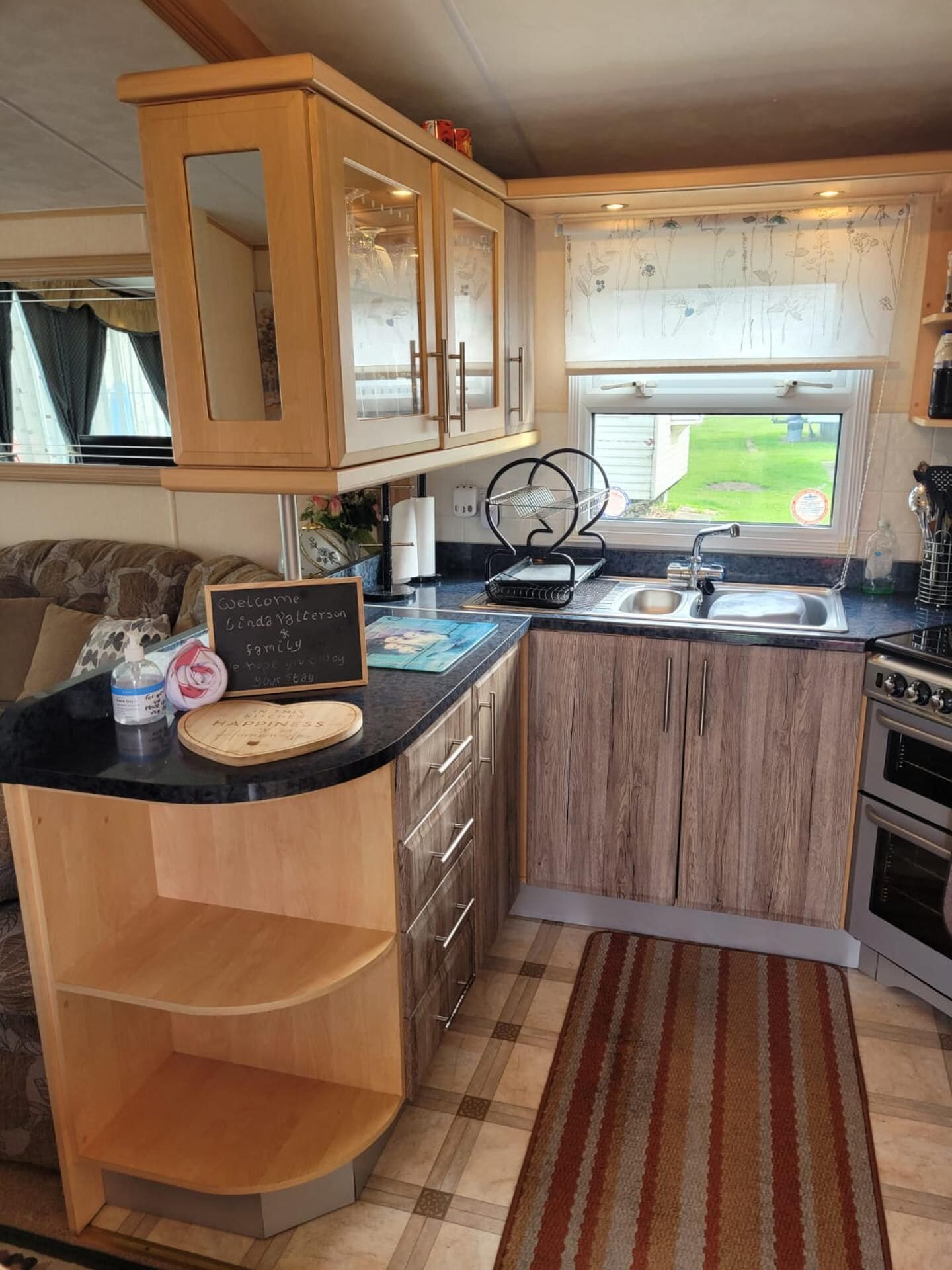 A compact kitchen with wooden cabinets, a built-in sink, a stove, and a window overlooking a yard.