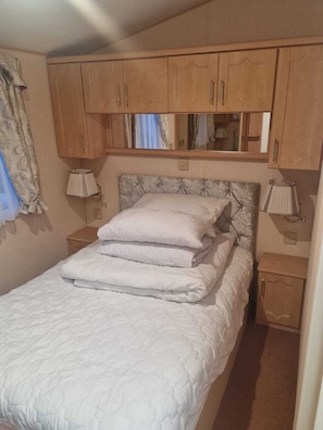 A bedroom with a bed, wooden cabinets, a mirror, and two bedside lamps. - Discover Comfort Home From Home 8-birth Caravan (Skegness)