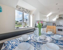 A dining area with a table set for four, a vase with flowers, and a view of the outside.
