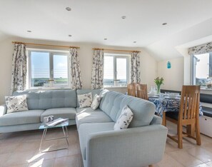 A living room with a grey sofa, a glass coffee table, and a dining area with a table and chairs. - Polmorla (Wadebridge)