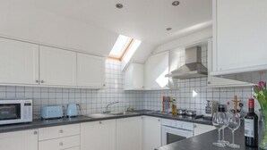 Una cocina moderna con armarios blancos, encimera negra, tragaluz y una botella de vino sobre la encimera.