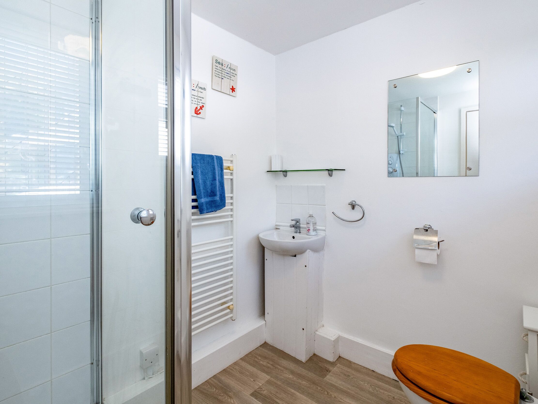 Een kleine, moderne badkamer met een douchegordijn van glas, een witte wastafel, een spiegel en een houten toiletbril.