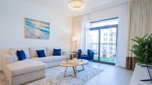 Un salon moderne avec un canapé blanc, des coussins bleus, une table basse et une grande fenêtre donnant sur des immeubles.