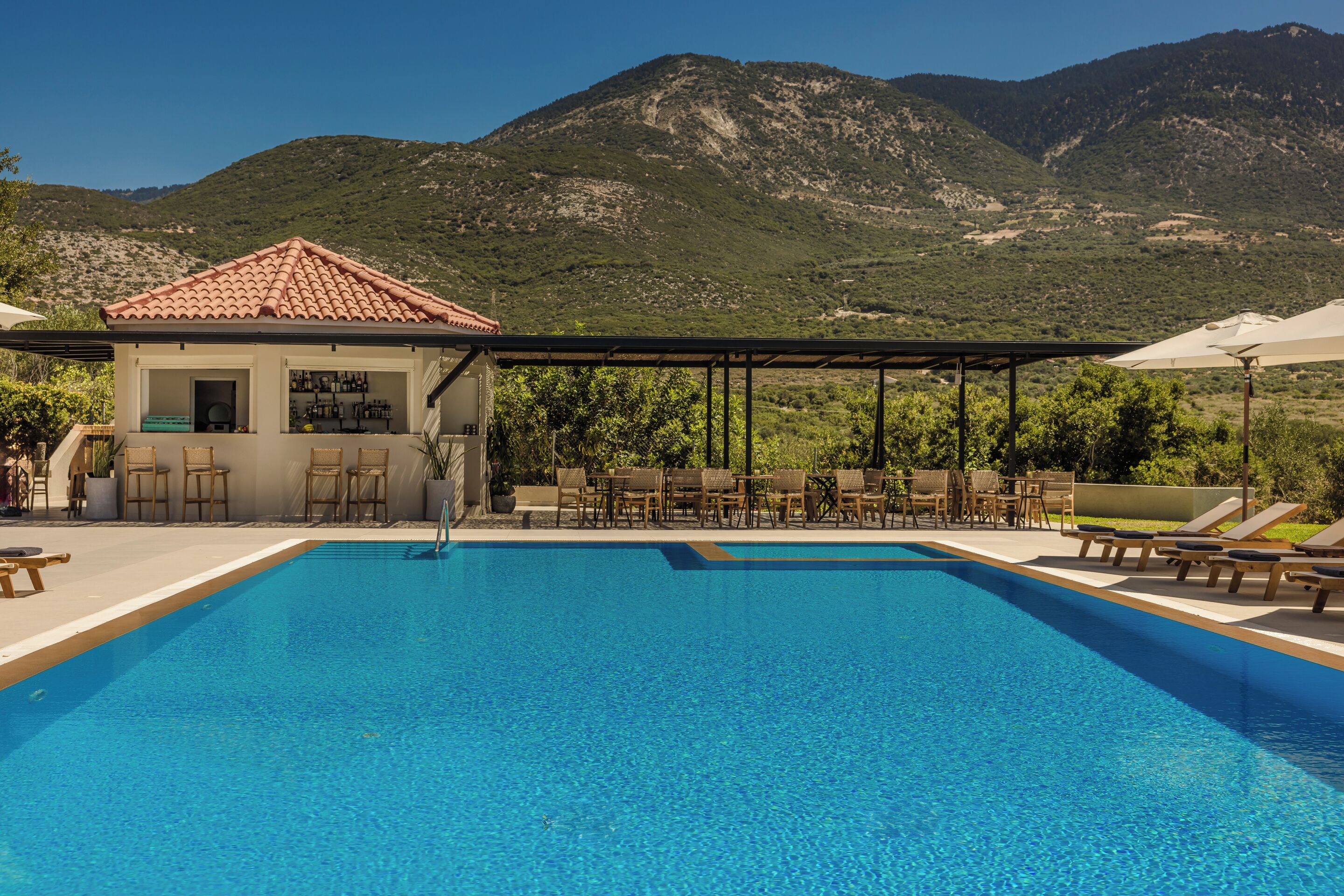 A swimming pool with lounge chairs and a bar area, surrounded by mountains.