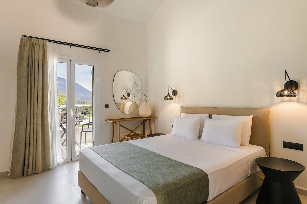 Quarto de hotel com cama, escrivaninha, cadeira, mesa, abajur e vista para o exterior.