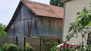 Ein Grill auf einer Tischplatte mit Metallgestell, ein Holzgebäude im Hintergrund und ein Blumentopf.