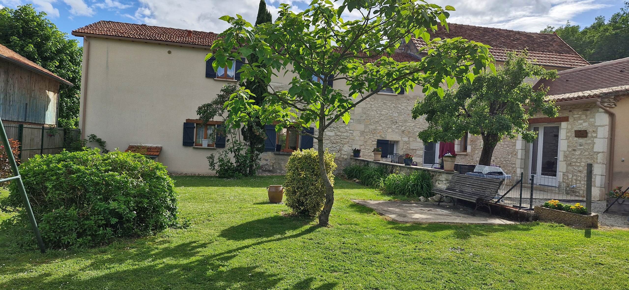 Ein zweistöckiges Haus mit Naturstein-Fassade, Ziegeldach und einem gepflegten Garten mit Bank und Pflanzkübeln.