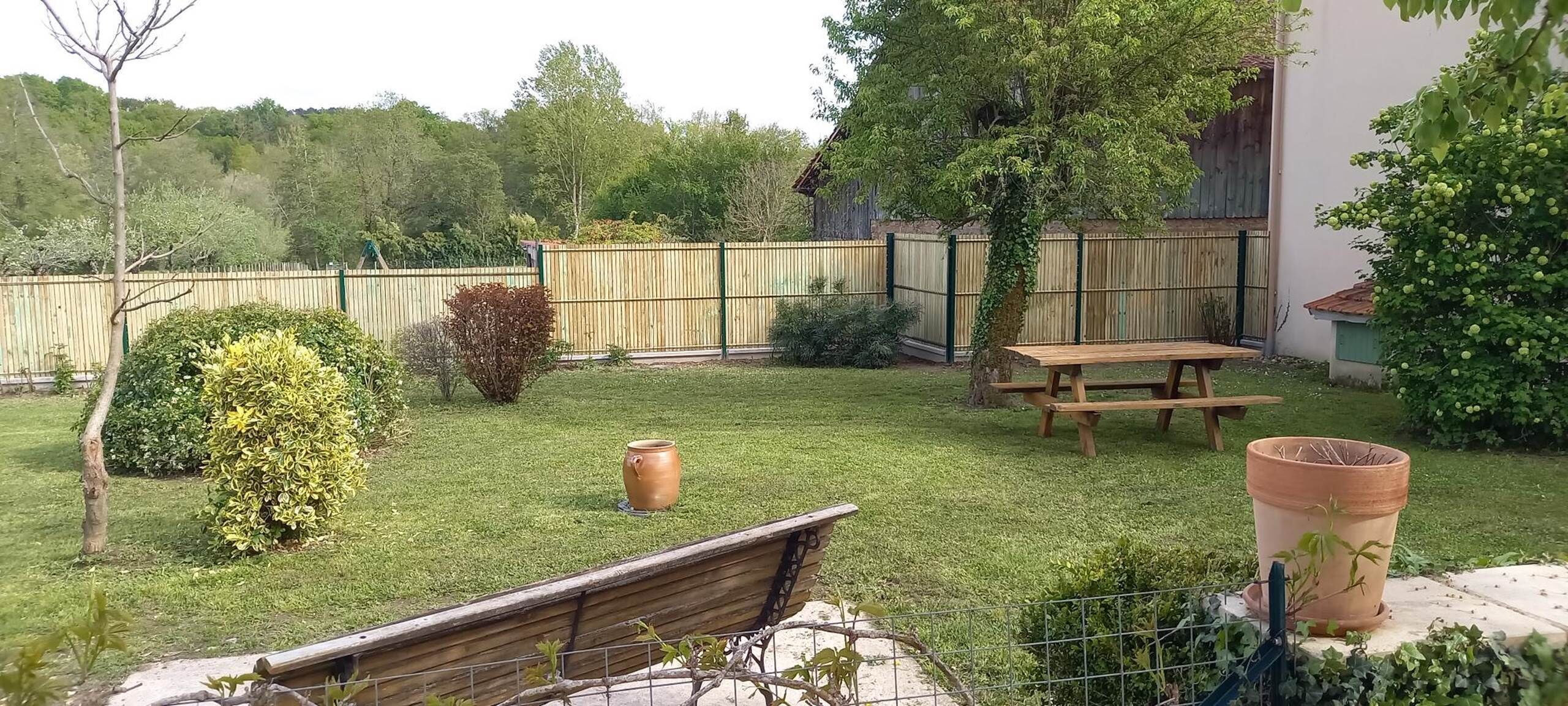 Un patio trasero con una mesa de madera, una planta en maceta y un área cercada.