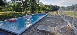 Una piscina rectangular con borde blanco, rodeada de grava, con dos sillas de descanso y un pequeño flotador inflable.
