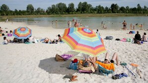 Ein Strand mit badenden und sonnenden Personen. Bunte Sonnenschirme spenden Schatten.