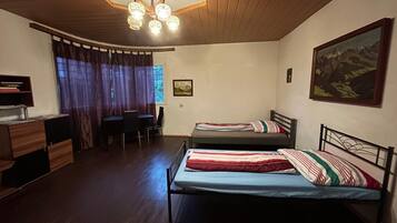 Une chambre avec deux lits, un bureau, une chaise, une bibliothèque et un tableau au mur.