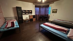 A room with two beds, a desk, a chair, a bookshelf, and a window with curtains.