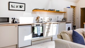 Ett kompakt kök med mikrovågsugn, brödrost och diskmaskin från Bosch. Ovanför diskhon finns en hylla i trä där tallrikar och glas förvaras. En inramad tavla hänger på väggen ovanför hyllan.