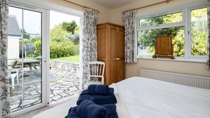 A bedroom with a bed, a wooden wardrobe, a chair, and a view of the garden through a sliding glass door. - Pencreek (Wadebridge)