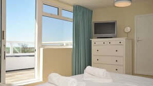 Une chambre d’hôtel avec un lit, un téléviseur posé sur une commode, une fenêtre avec des rideaux et une vue sur l’extérieur.