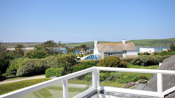 Une vue sur la côte, prise depuis un balcon, avec un ciel dégagé, une maison en pierre et une étendue d'eau en arrière-plan.
