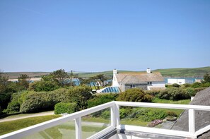 Uitzicht op de kust vanaf een balkon, met een heldere lucht, een stenen huis en een waterpartij op de achtergrond.