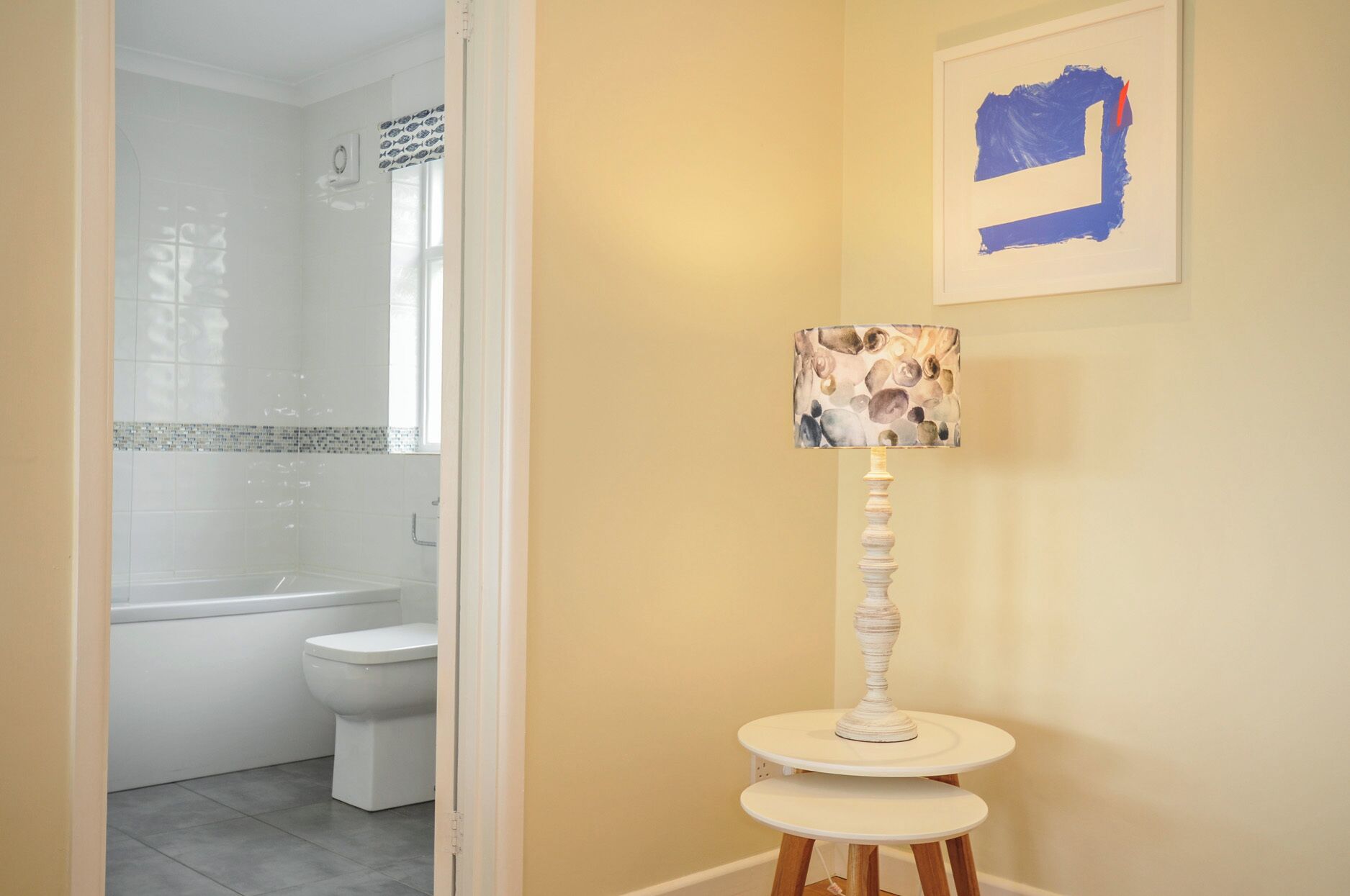 A bathroom with a toilet, a shower, and a small table with a lamp.