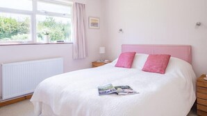 A bedroom with a large bed, a window with curtains, a bedside table, and a radiator. - Rosevallen (Wadebridge)