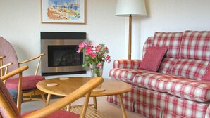 A living room with a plaid sofa, wooden chairs, a small round table, a fireplace, and a lamp. - Rosevallen (Wadebridge)