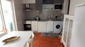Une cuisine compacte avec des meubles blancs, un four encastré, un four à micro-ondes et un lave-linge.
