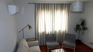 Un salon comprenant un canapé, deux fauteuils, une table basse, une lampe, une plante en pot et une fenêtre avec des rideaux.