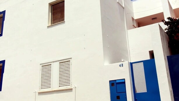 Un bâtiment blanc avec une porte bleue et des volets bleus aux fenêtres, une petite fenêtre et le numéro « 42 » peint sur le mur.